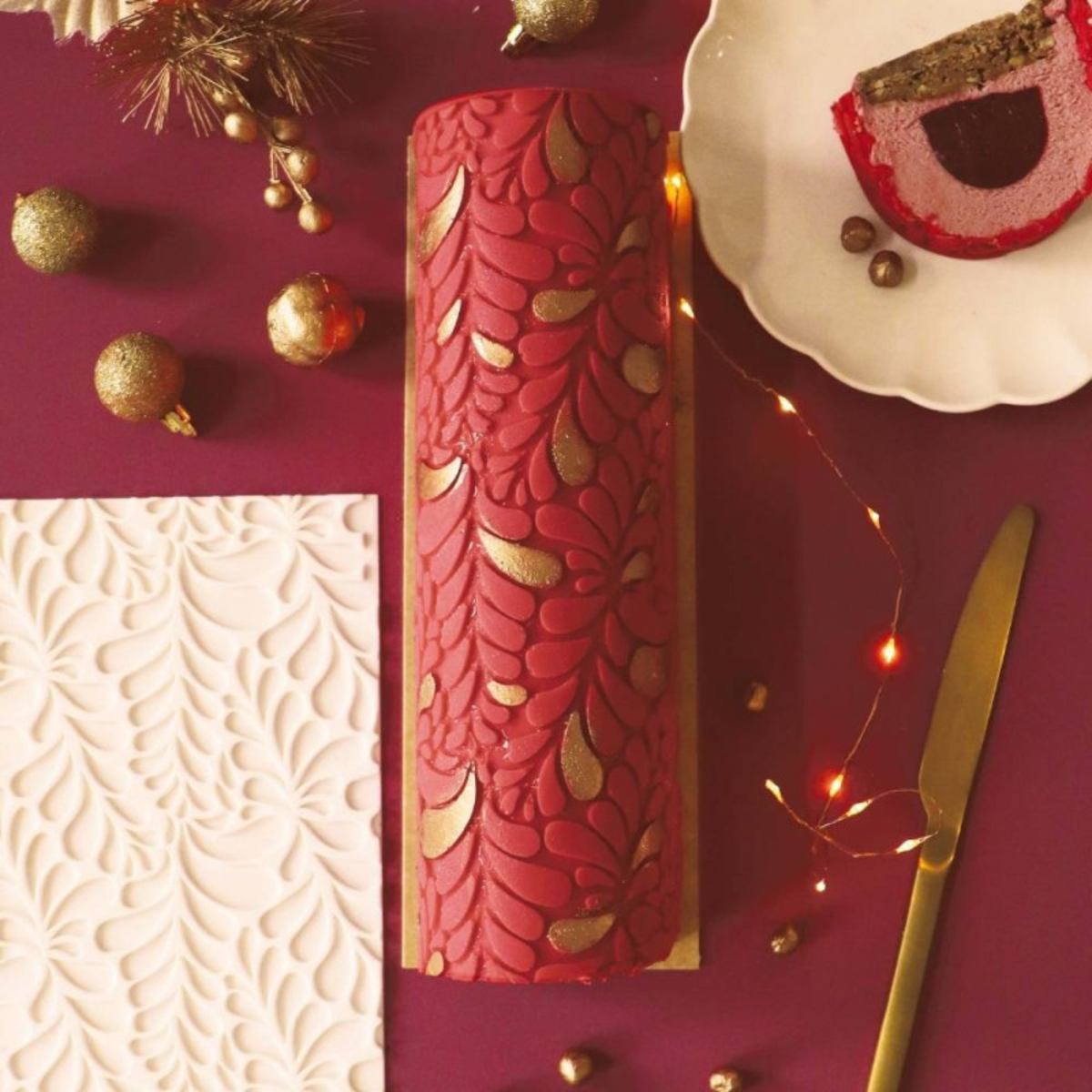 Bûche de Noël rouge décorée de motifs végétaux en relief et de touches dorées grâce au tapis silicone ScrapCooking Cookina