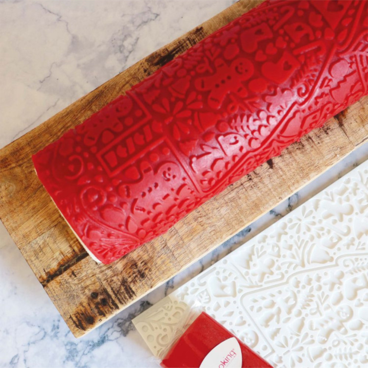 Gros plan sur une bûche de Noël rouge aux motifs festifs en relief, accompagnée du tapis silicone blanc ScrapCooking Cookina.
