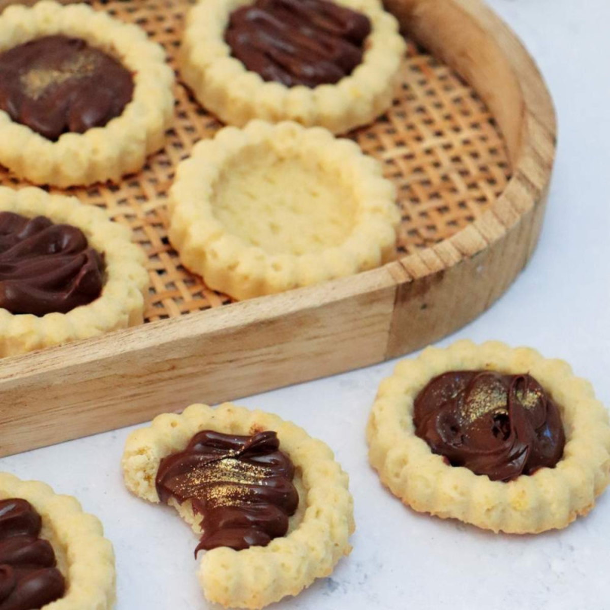 Mini-tartelettes dorées garnies de chocolat fondant avec touches dorées, présentées sur un plateau en bois.