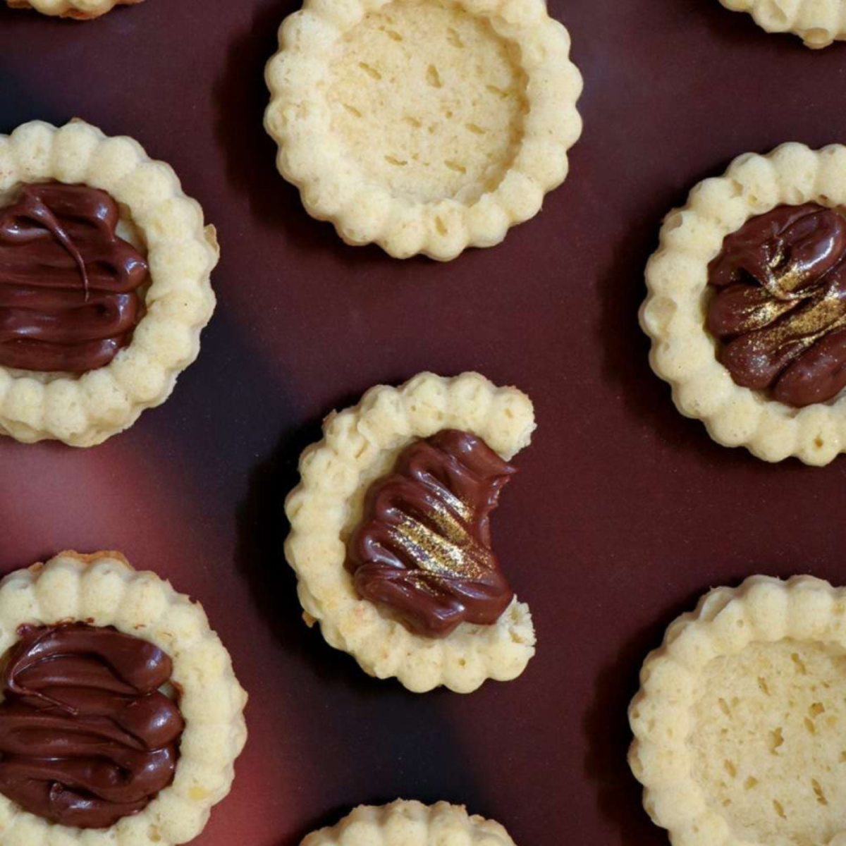 Assortiment de mini-tartelettes maison aux bords cannelés, nature ou garnies de chocolat avec décorations dorées.