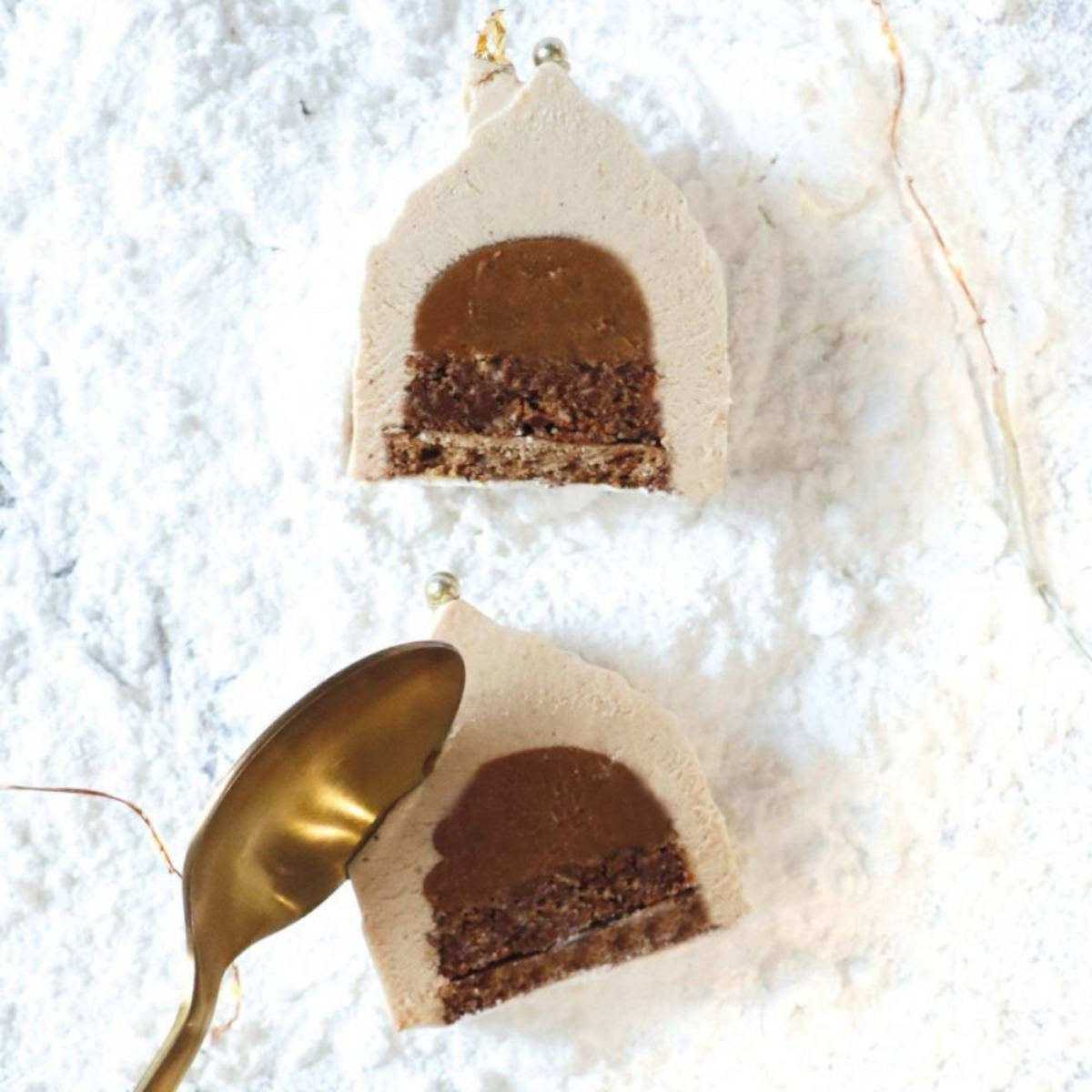 Deux entremets individuels en forme de chalets de Noël, coupés en deux pour dévoiler leurs différentes couches de mousse, chocolat et biscuit.