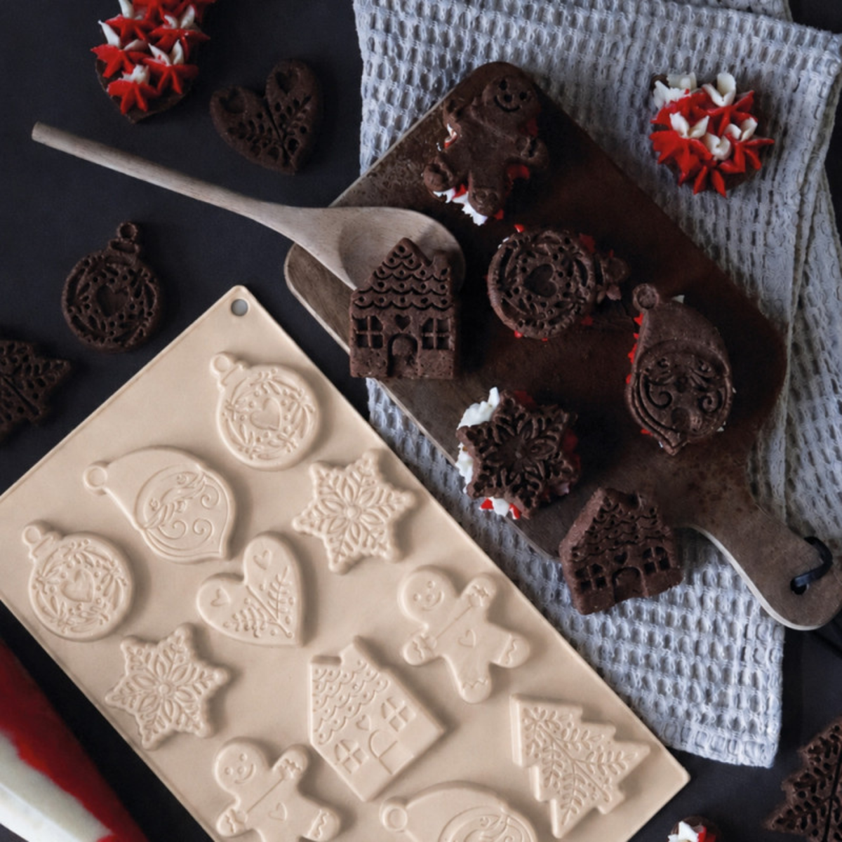 Moule silicone ScrapCooking pour biscuits de Noël accompagné de biscuits au chocolat en forme de sapins, maisons, flocons et bonhommes en pain d'épices.