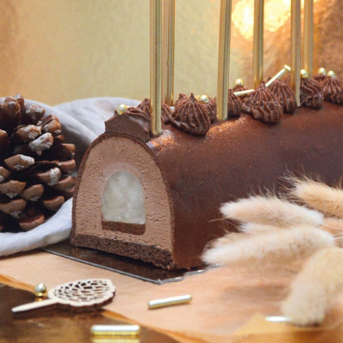 Bûche de Noël au chocolat réalisée dans un moule demi-rond, avec mousse chocolat, insert blanc et décoration de crème chocolat et perles dorées.