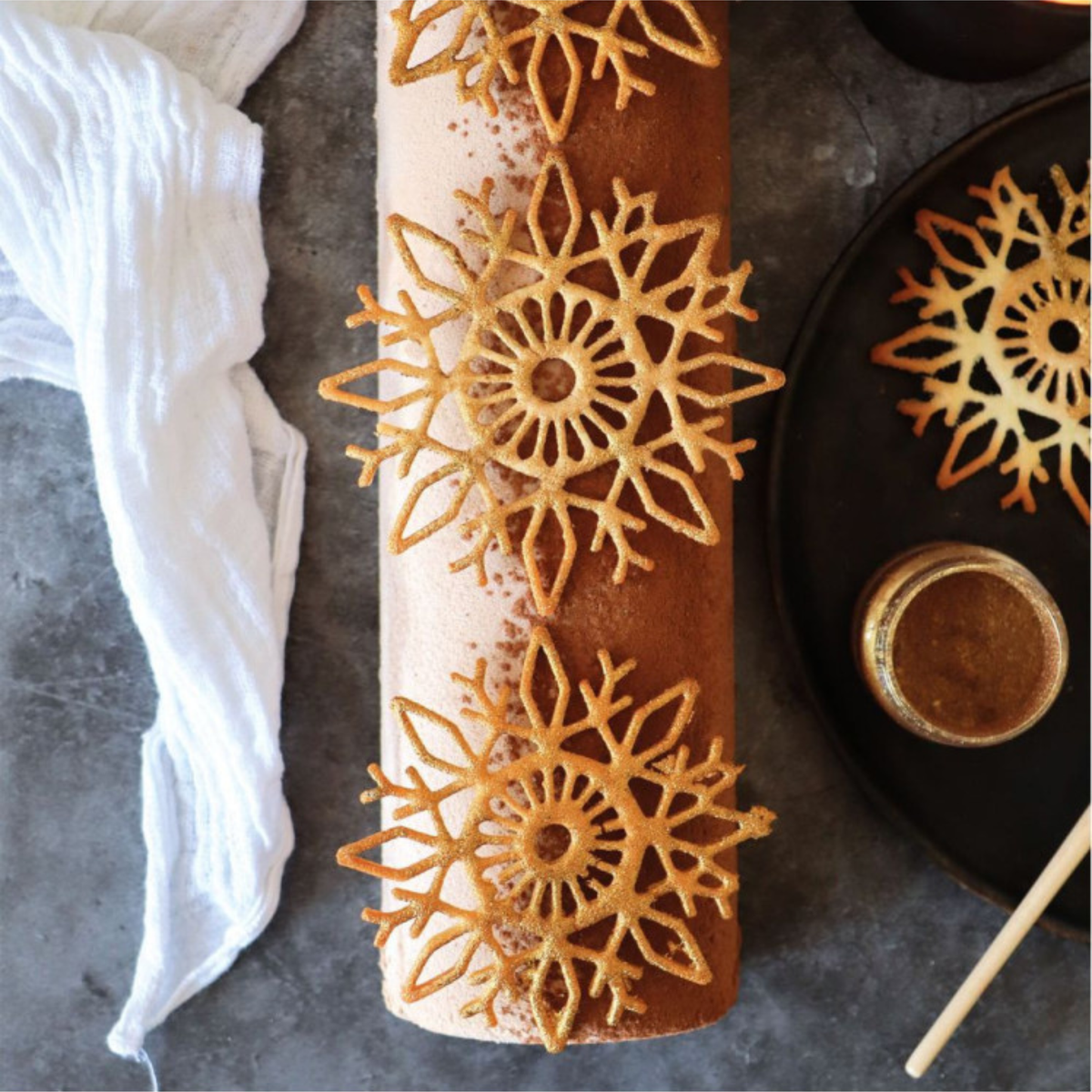 Bûche de Noël décorée de grands flocons de neige dorés réalisés avec le tapis en silicone ScrapCooking, présentée en vue de dessus.