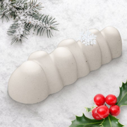 Bûche de Noël Mont Blanc blanche avec reliefs arrondis, décorée d’un flocon de neige, présentée avec des branches de sapin enneigées et des baies de houx rouges.